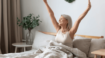 Happy woman stretching her arms upwards in bed