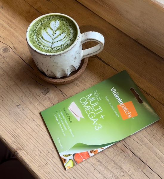 Matcha latte in a ceramic mug next to an Adult Multi + Omega-3 Patch on a wooden table.