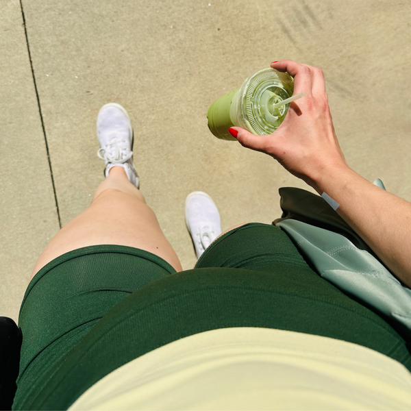 A person walking outdoors holding a fruit drink and wearing a patch on their wrist