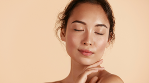 Woman with dark hair and glowing skin posing against a beige background.