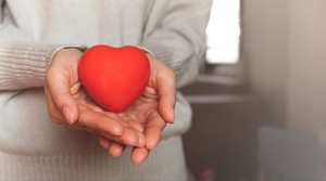 person wearing a grey jumper holding a red, foam heart in their hands.