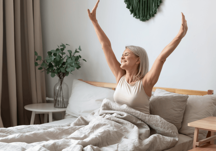 Happy woman stretching her arms upwards in bed