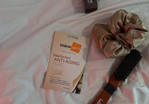 VitaRenew Anti-Aging Plus Patch pack placed on a bed beside a satin scrunchie and a wooden hairbrush.