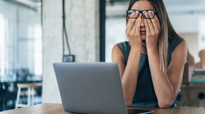 A woman in an office. she is sat in front of a computer and looks tired.