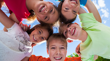 Happy children gathered in a circle and a clear blue sky behind them
