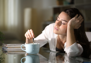 Woman looking tired while stirring coffee at a table indoors