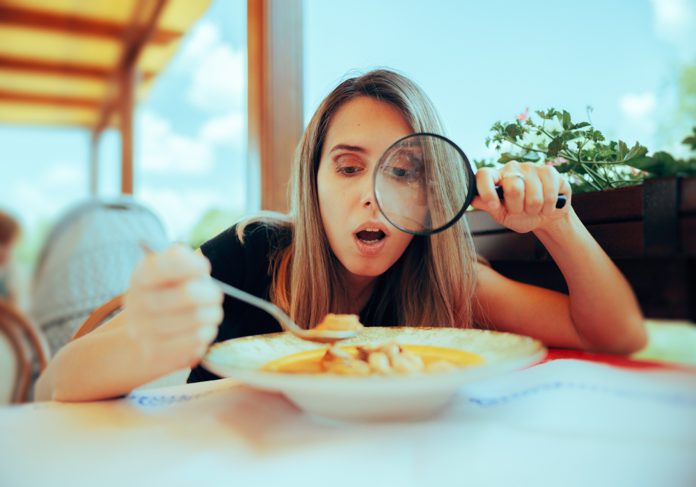 Woman using a magnifying glass to examine her food at an outdoor dining table.